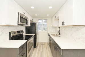 Contemporary kitchen featuring white upper cabinetry, dark lower cabinetry, light countertops, a white subway tile backsplash, and stainless steel appliances