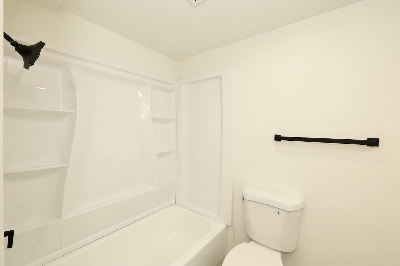 White bathtub and shower combination unit featuring an integrated shower head and shelving