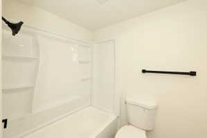 White bathtub and shower combination unit featuring an integrated shower head and shelving