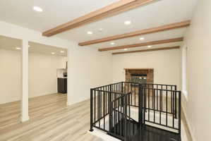 Living area featuring wood-finish flooring, exposed ceiling beams, recessed lighting, and a spiral staircase with black metal railing