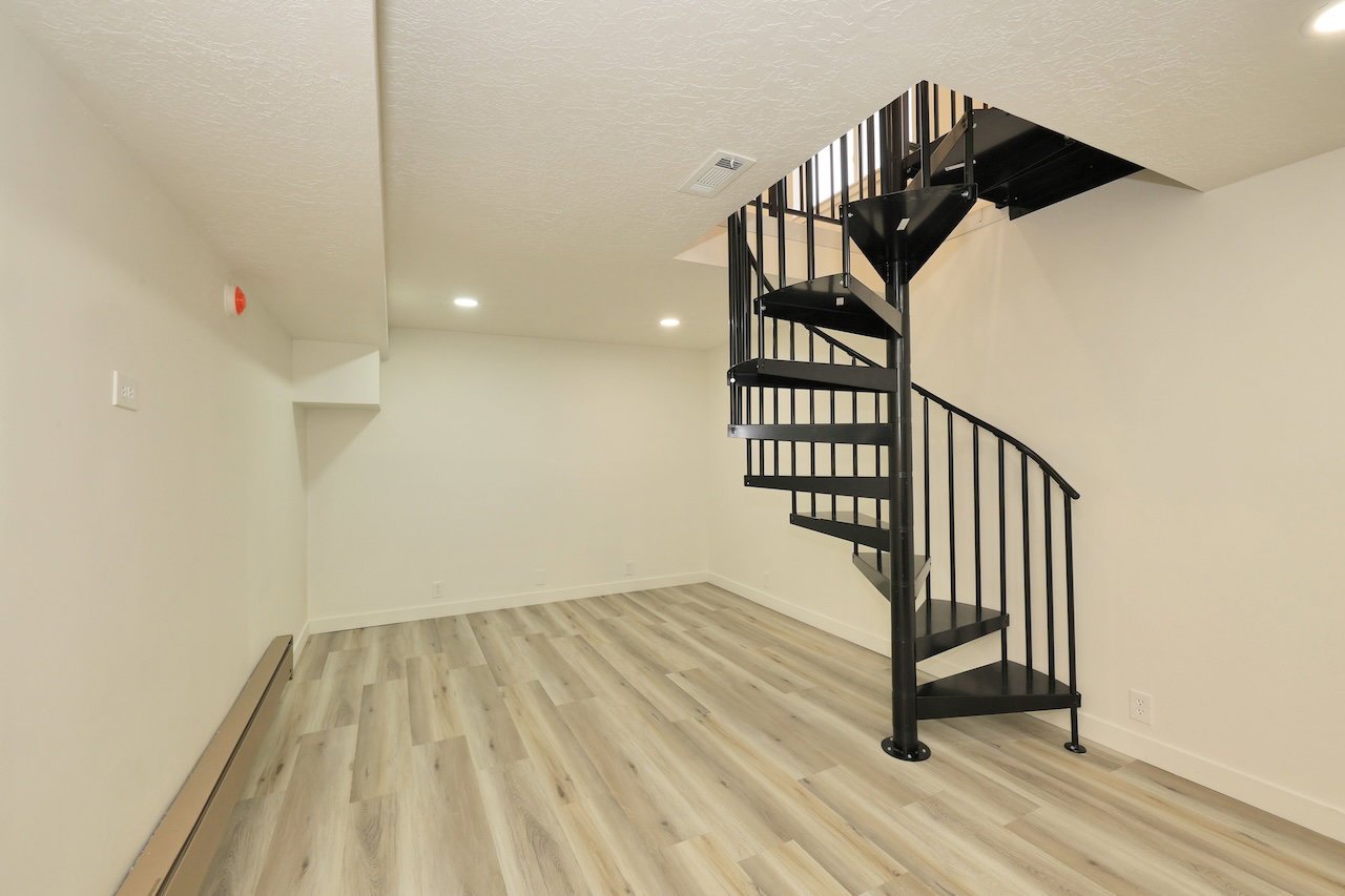 Expansive room featuring a black spiral staircase with metal balusters, wood-finish flooring, recessed lighting, and crisp white walls