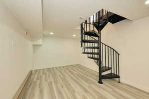 Expansive room featuring a black spiral staircase with metal balusters, wood-finish flooring, recessed lighting, and crisp white walls