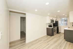 Contemporary kitchen featuring stainless steel appliances, light wood-finish flooring, recessed lighting, white upper cabinetry, and dark lower cabinetry