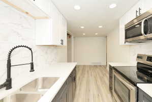 Modern kitchen featuring white upper cabinetry, dark lower cabinetry, light countertops, a double stainless steel sink with a matte black faucet, and a subway tile backsplash