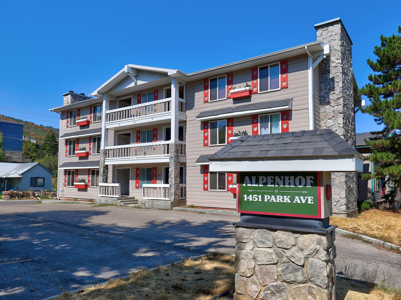 Three-story multi-unit building featuring balconies, red shutters, and stone accents