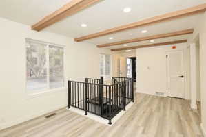 Expansive open-concept room featuring wood-finish flooring, exposed wood ceiling beams, and recessed lighting