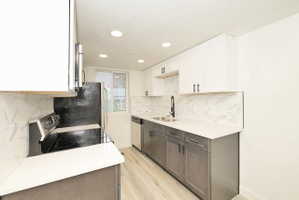Modern kitchen featuring white upper cabinetry, gray lower cabinetry, light wood-finish flooring, white countertops, and a marble-patterned tile backsplash