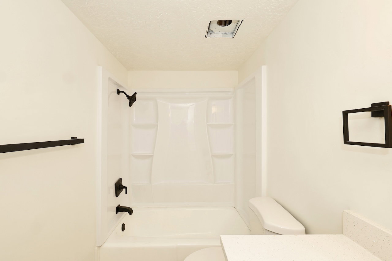 Bathroom with white fiberglass tub and shower surround, matte black fixtures, white walls, and a white countertop