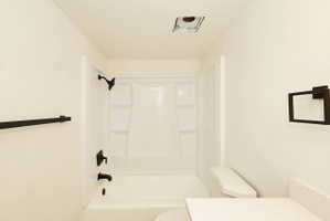 Bathroom with white fiberglass tub and shower surround, matte black fixtures, white walls, and a white countertop