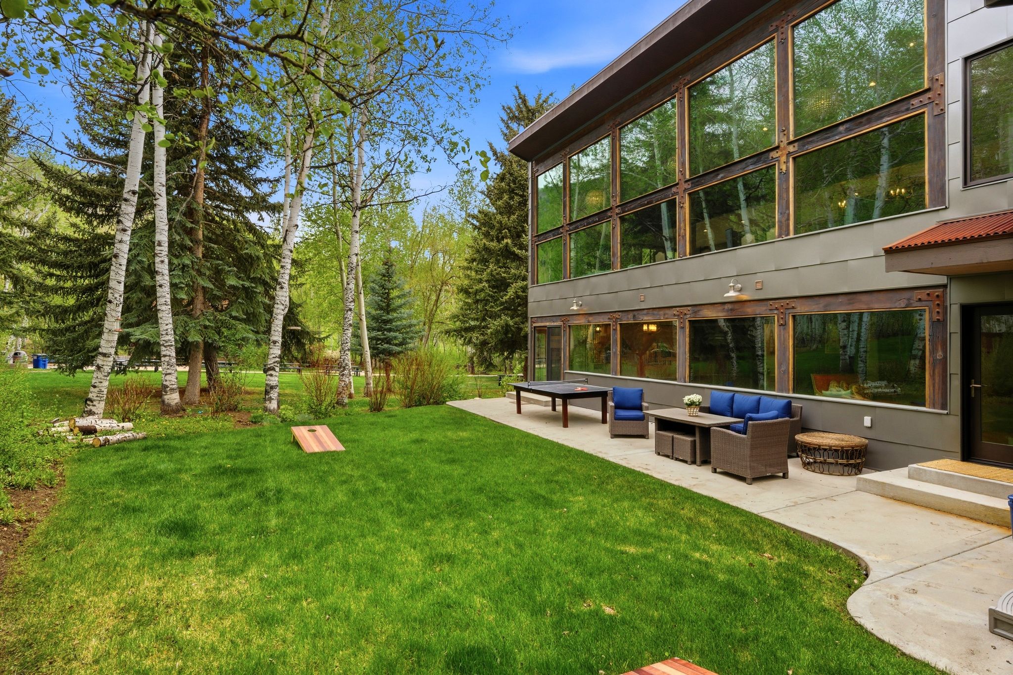 Contemporary exterior with expansive floor-to-ceiling windows, a large concrete patio, and a manicured lawn