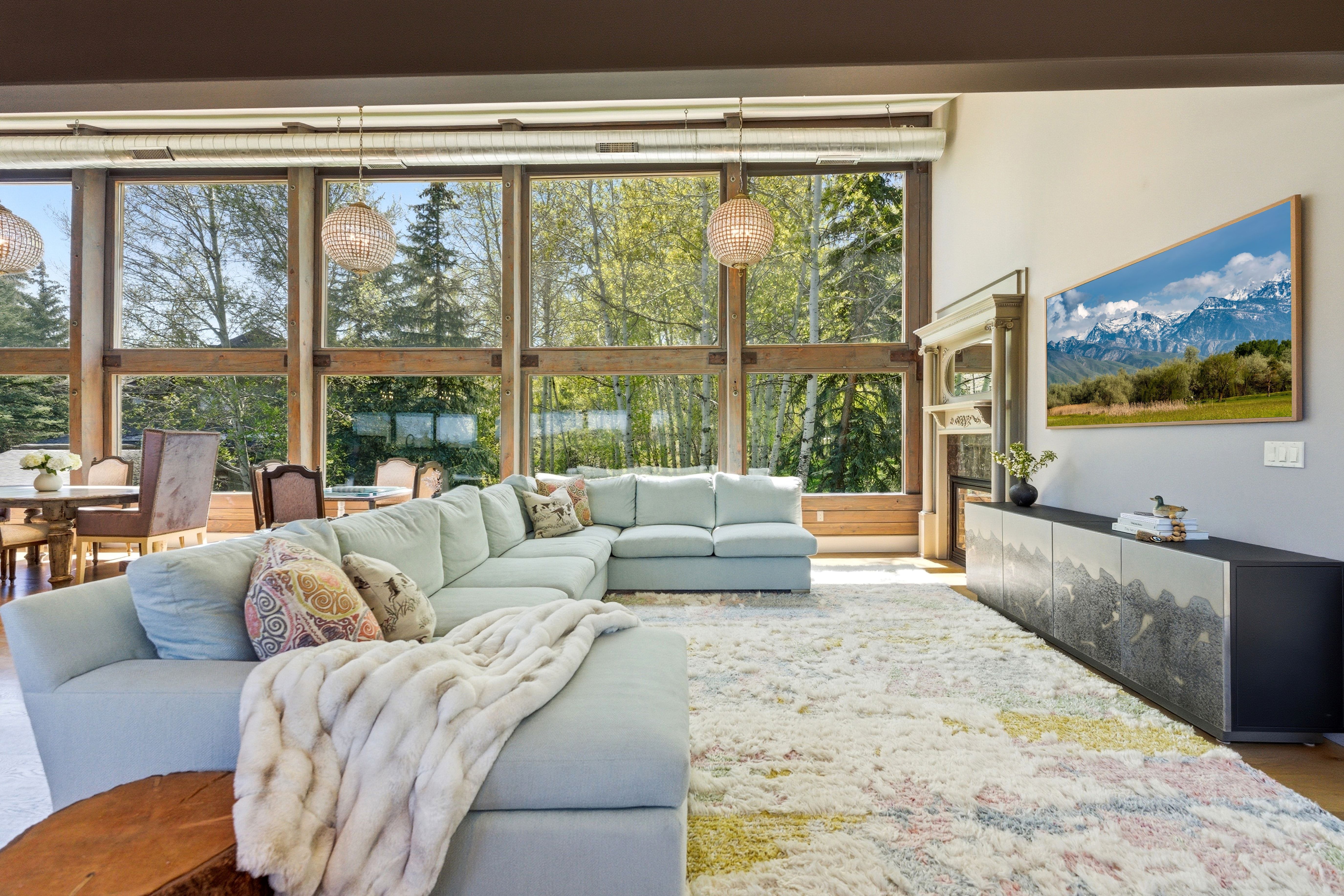 Floor-to-ceiling windows with wood framing, two woven pendant light fixtures, and a decorative fireplace surround with mantel