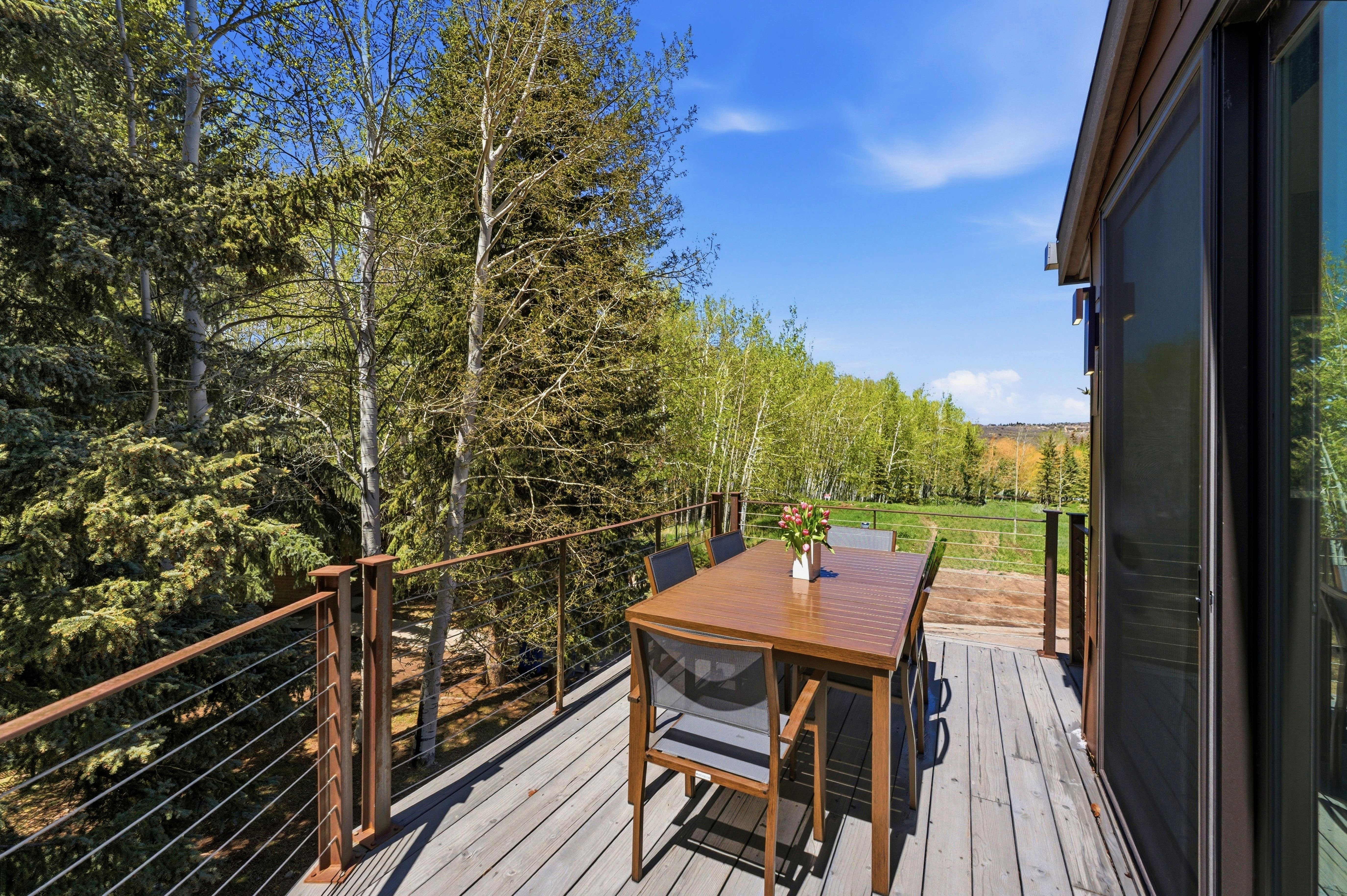 Exterior deck featuring wood-finish flooring, metal railing with horizontal cable infill, and a sliding glass door