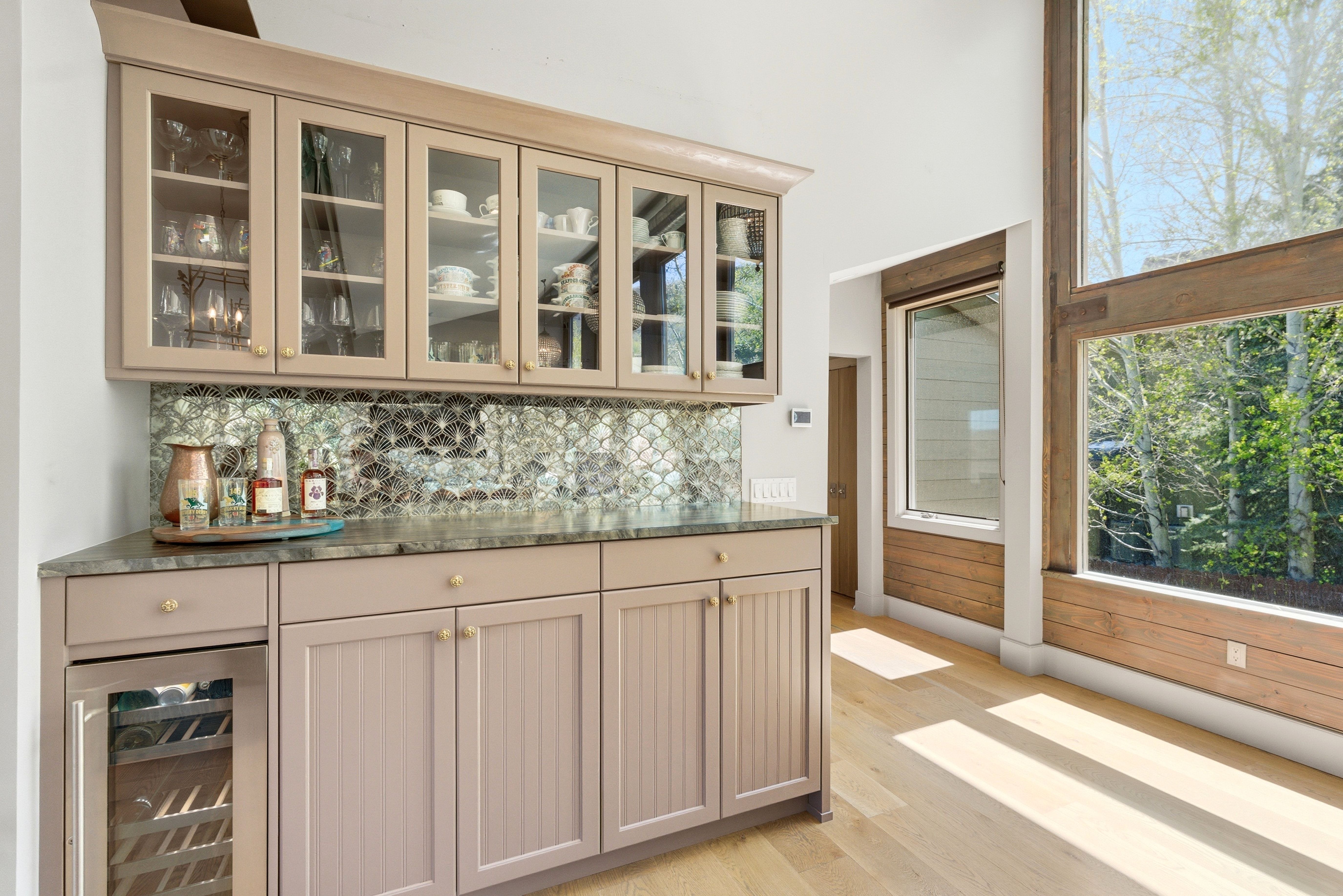 Built-in wet bar featuring upper glass-front cabinetry, a scalloped tile backsplash, stone countertop, and an integrated beverage refrigerator