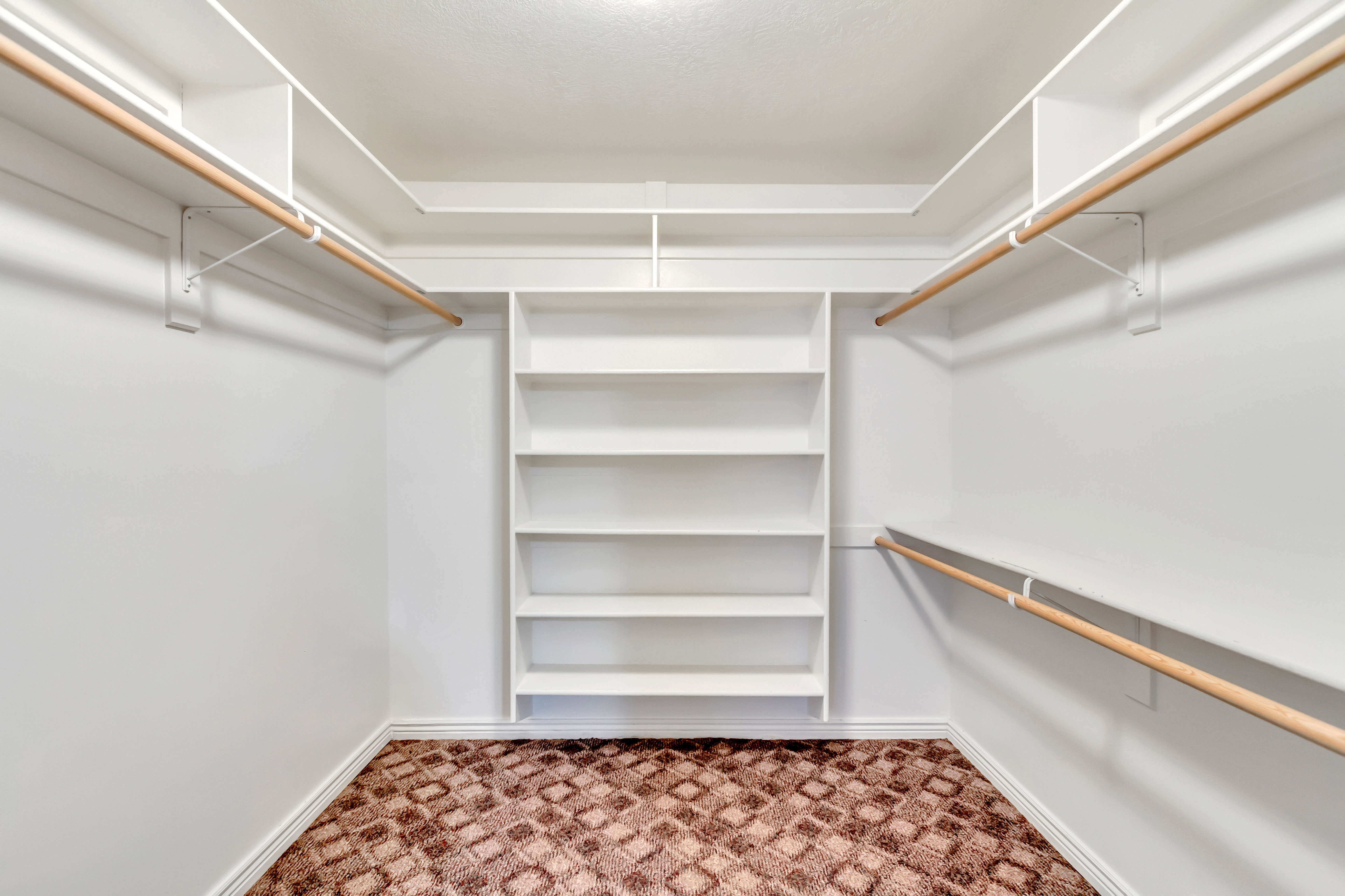 Walk-in closet featuring built-in shelving, dual hanging rods, white walls, white baseboards, and patterned carpet flooring