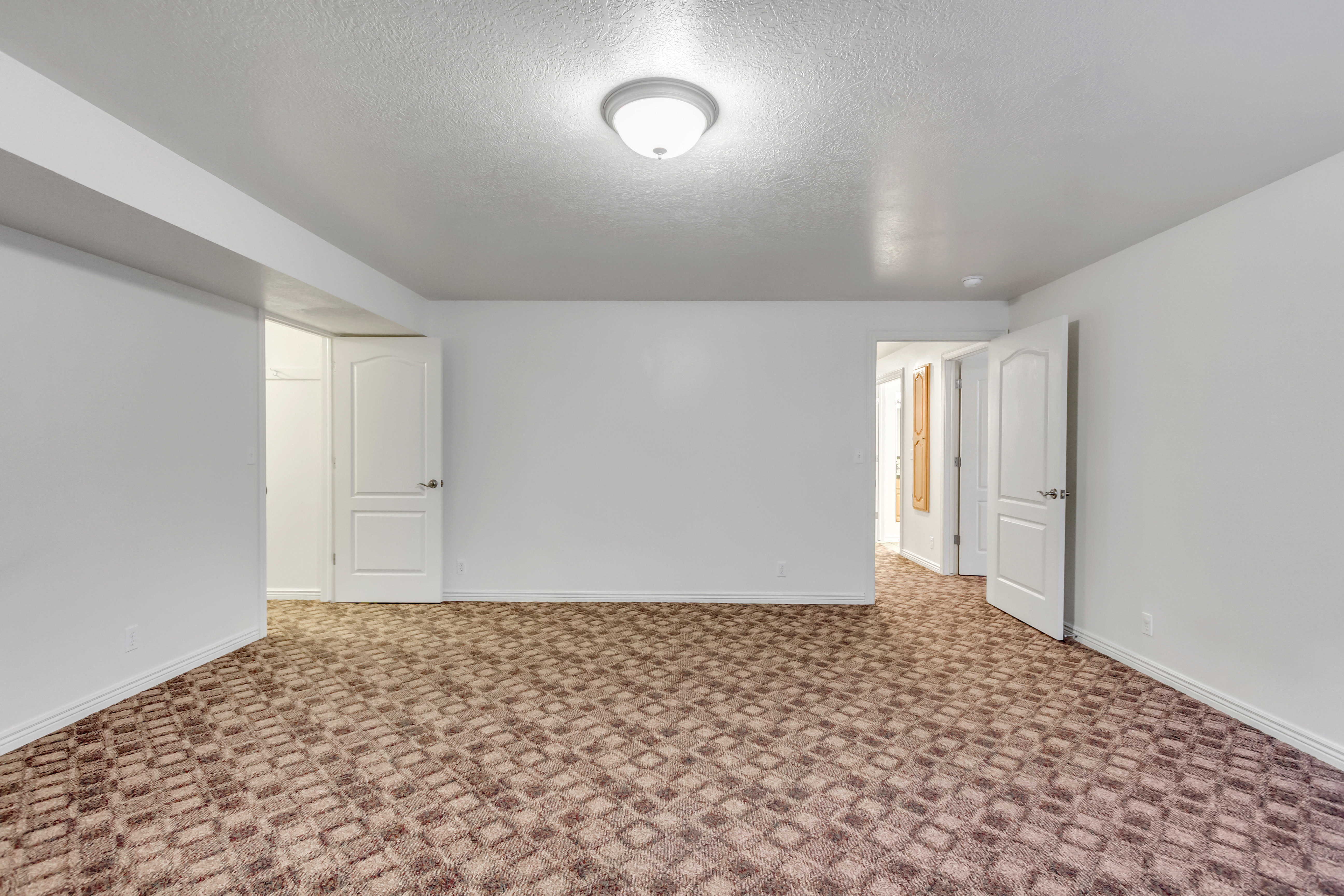 Spacious room featuring patterned carpeting, white walls, and a flush mount ceiling light