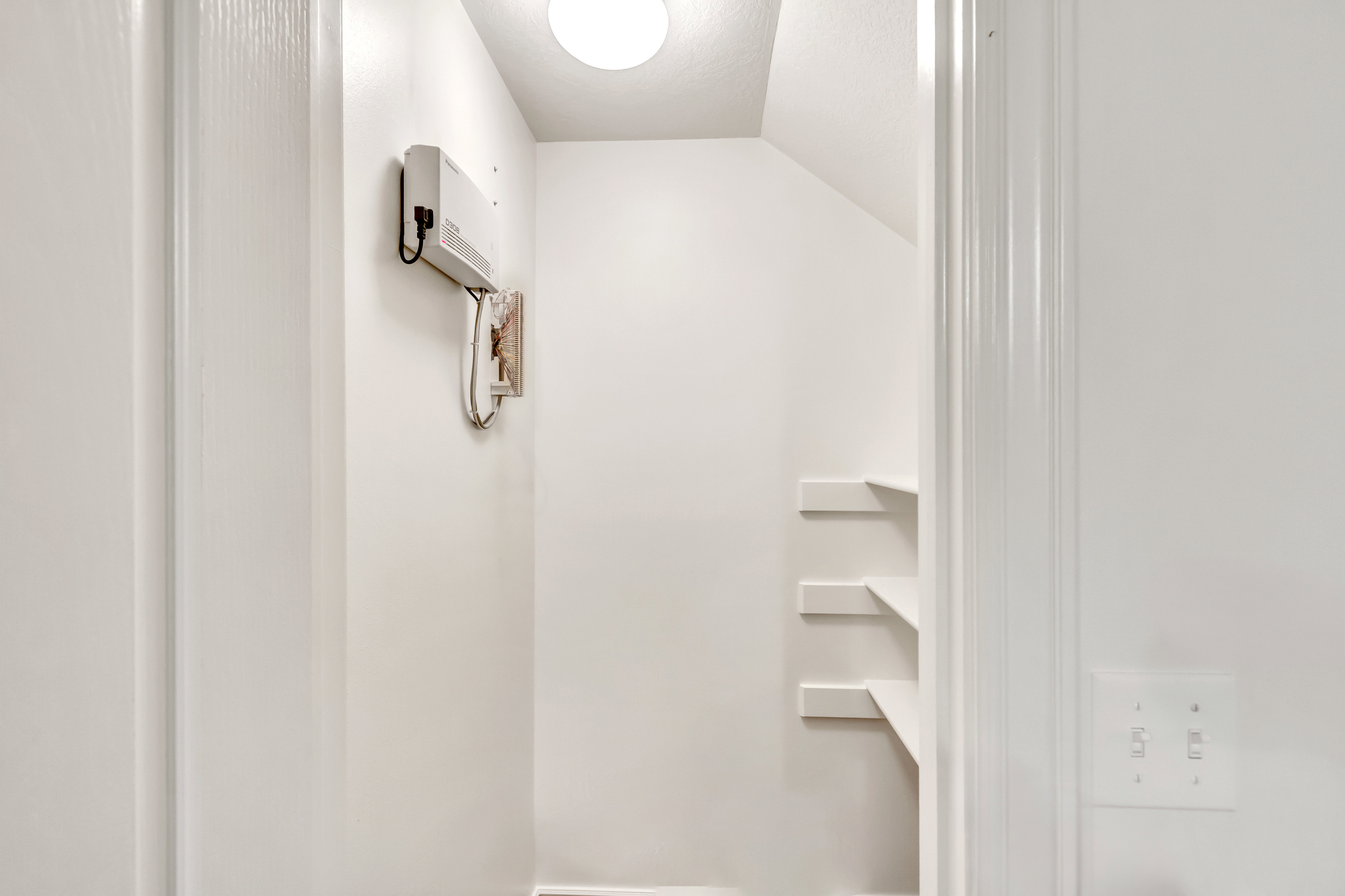 Under-stair storage area featuring multiple built-in shelves, white painted walls, and an overhead light fixture
