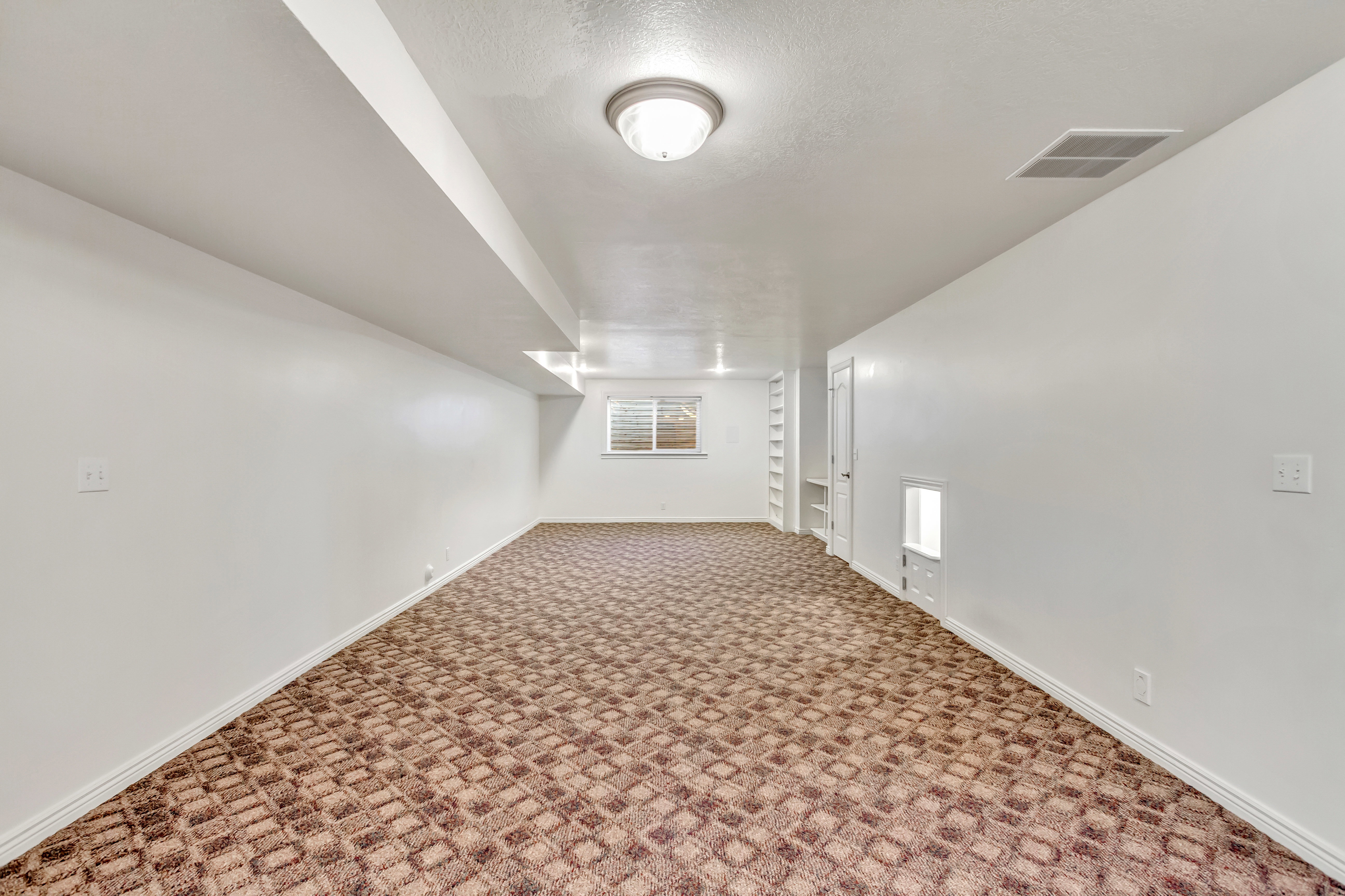 Spacious room featuring patterned carpet flooring, white painted walls, and a window with horizontal blinds