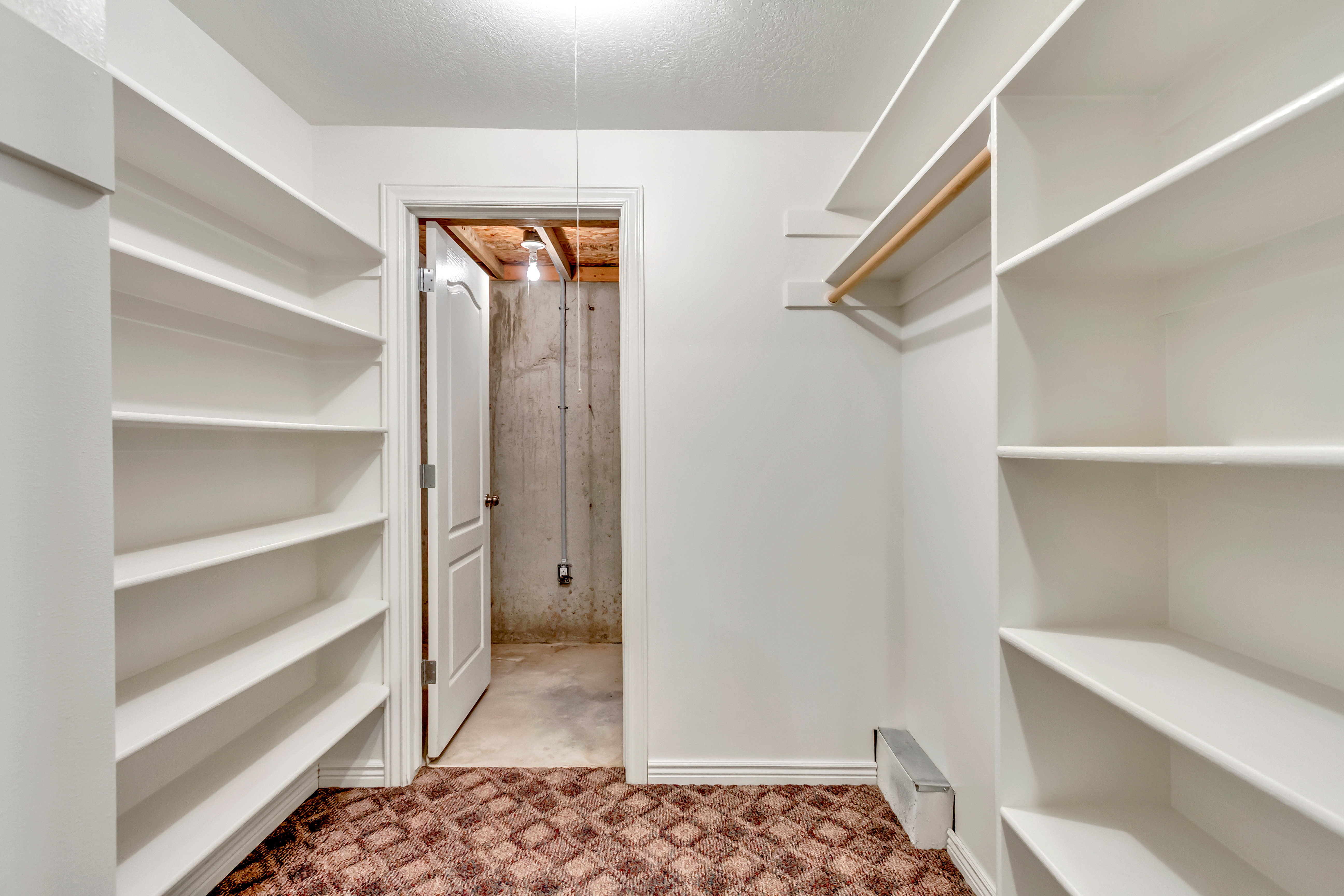 Walk-in closet featuring extensive built-in shelving, white walls, white trim, a clothes hanging rod, and a patterned carpet
