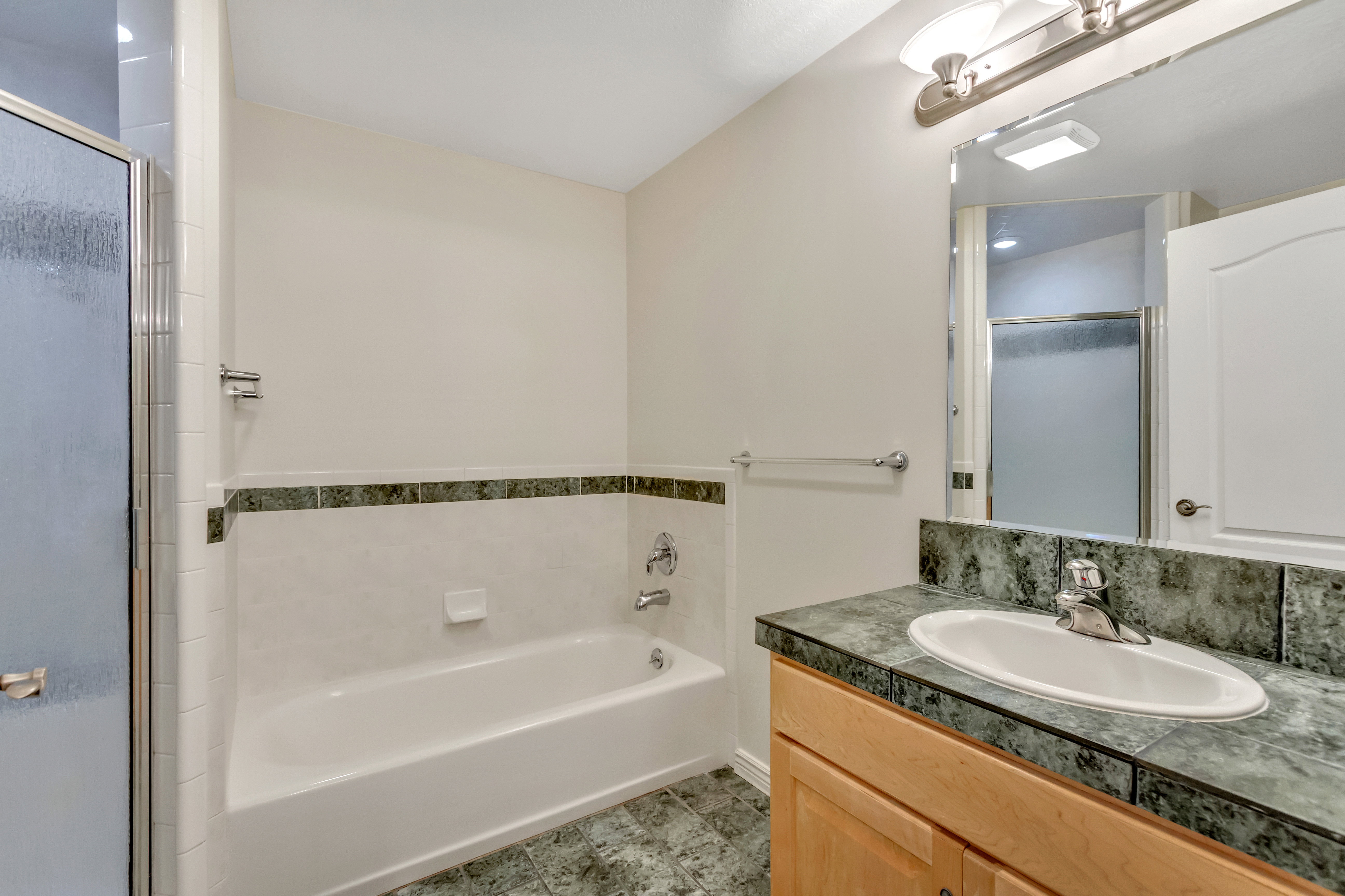Bathroom featuring a white bathtub, a glass-enclosed shower, a vanity with a drop-in sink, and a mirrored medicine cabinet