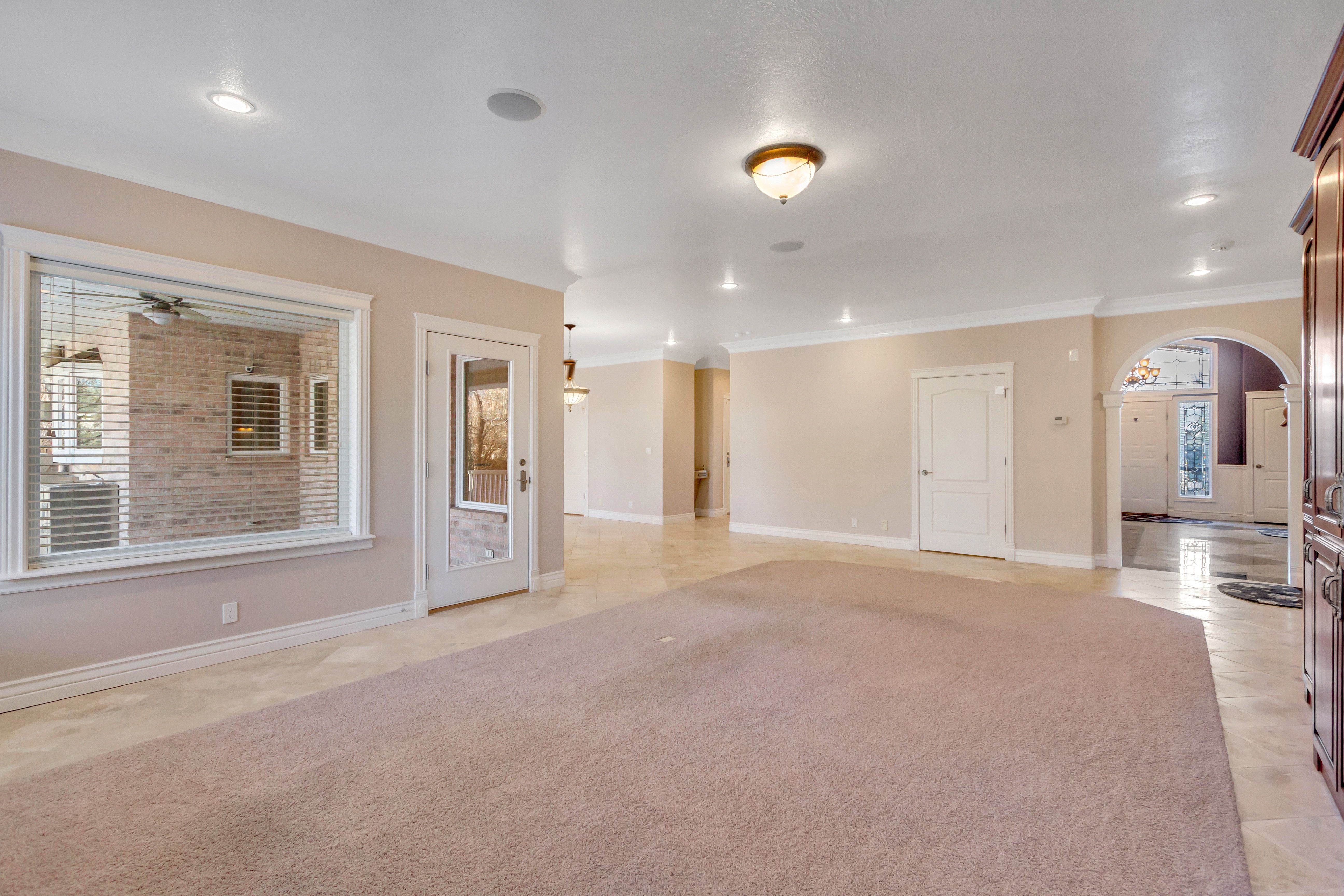 Expansive room featuring recessed lighting, a large window with horizontal blinds, and a glass-paneled door