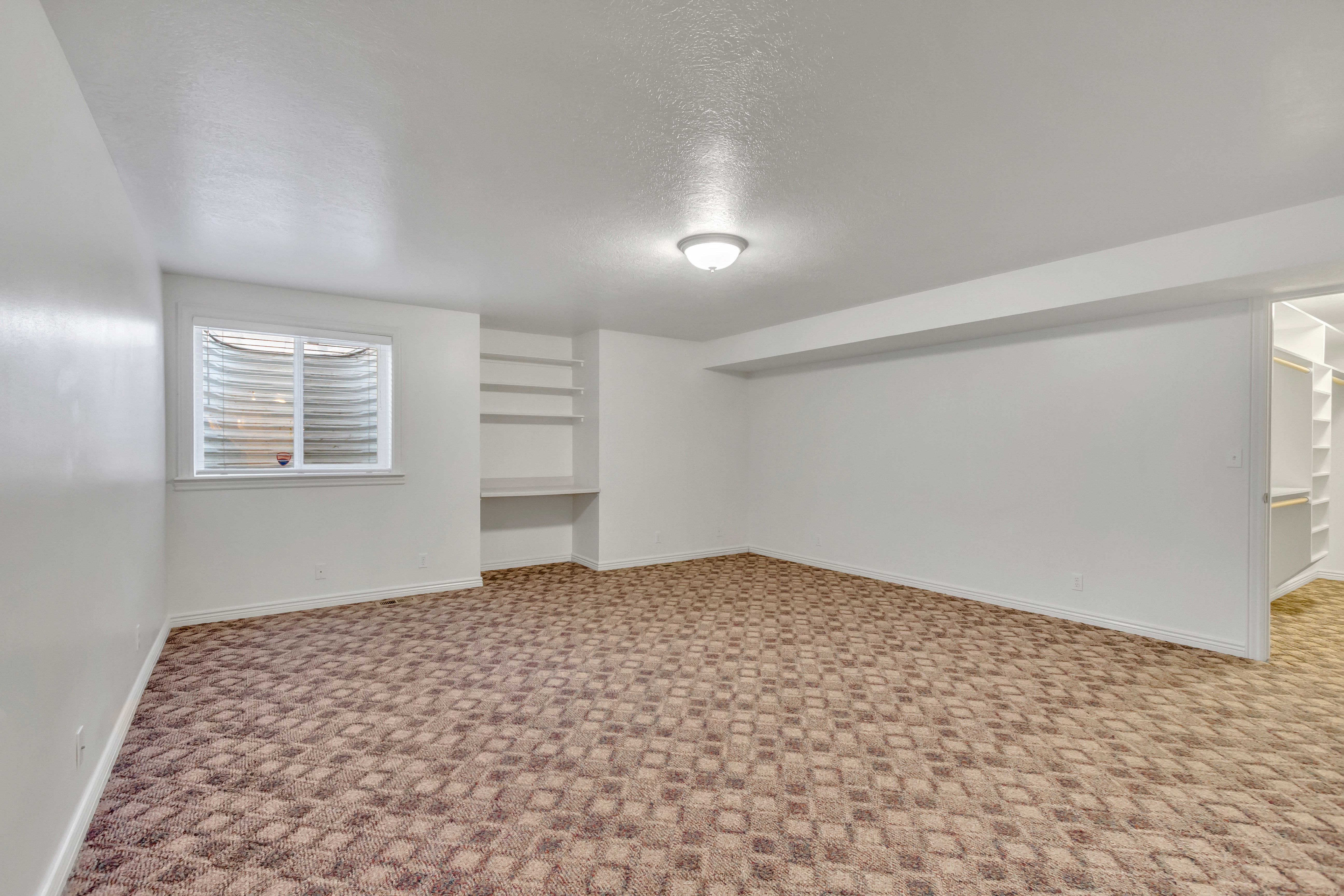 Spacious room featuring patterned carpeting, recessed ceiling light fixture, a window with horizontal blinds, built-in shelving, and a built-in closet system