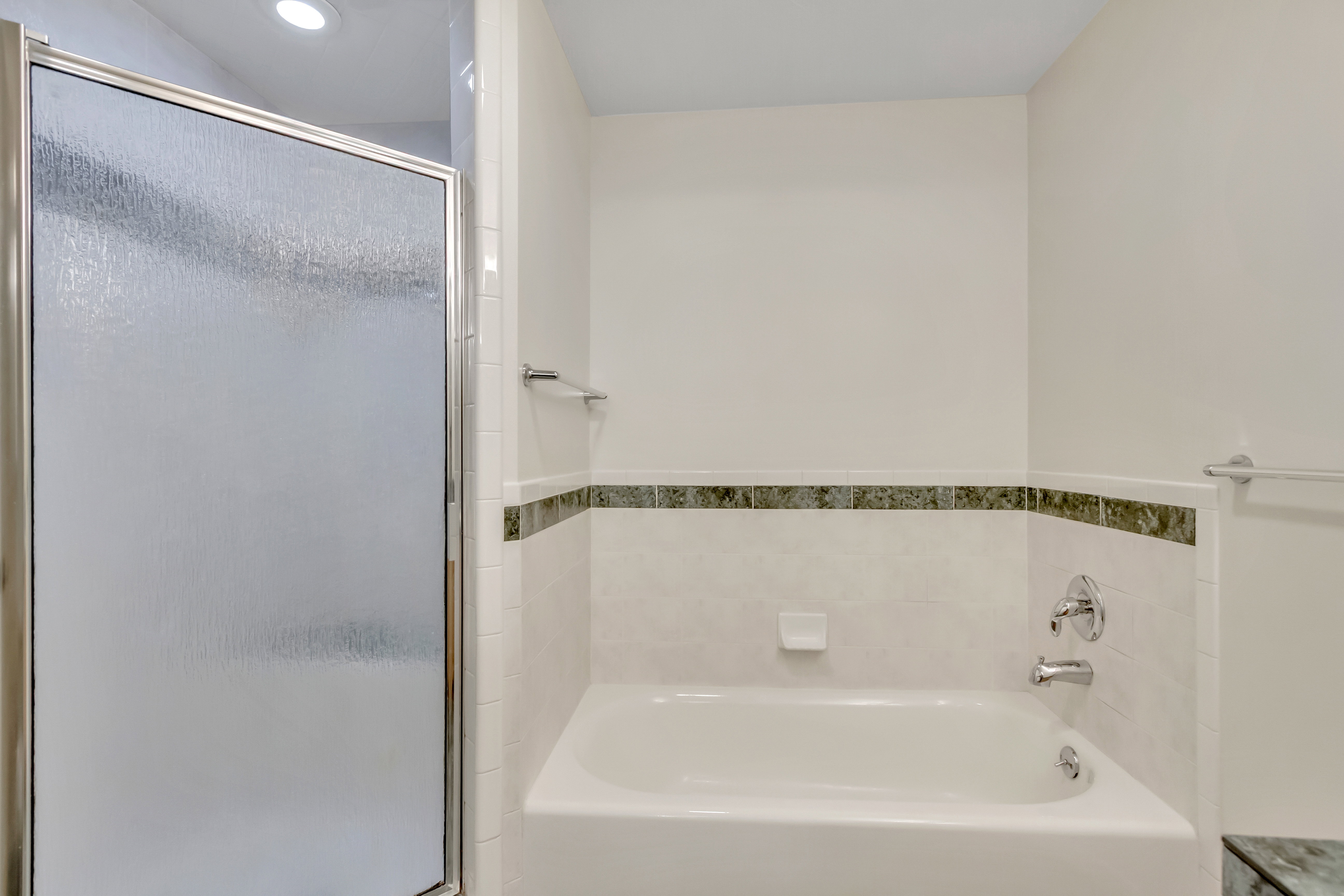 Shower-over-tub combination featuring a sliding glass door with a textured panel, chrome hardware, a tiled surround, a built-in soap dish, and a decorative tile accent band