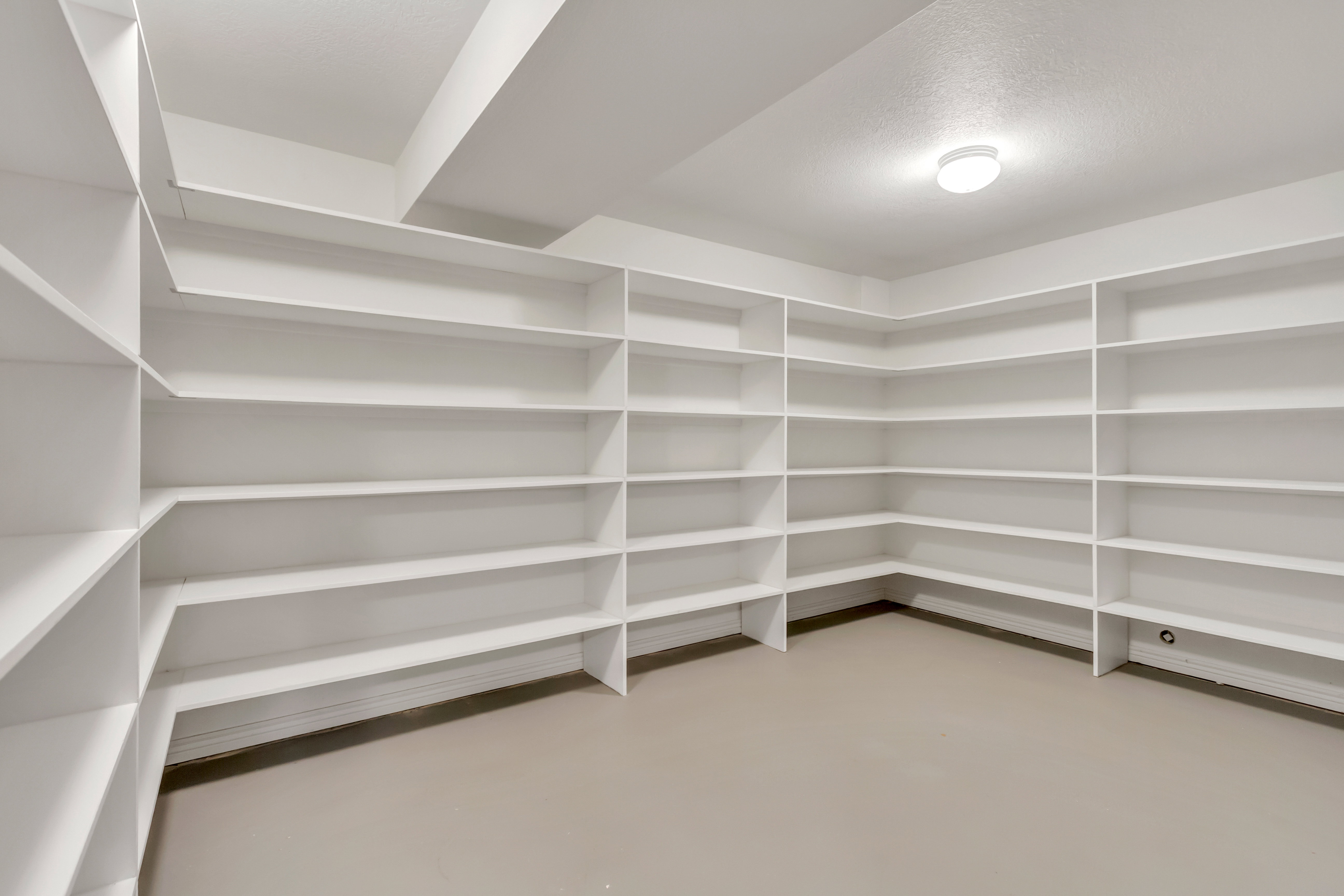 Spacious storage room featuring extensive built-in white shelving, recessed lighting, and neutral flooring