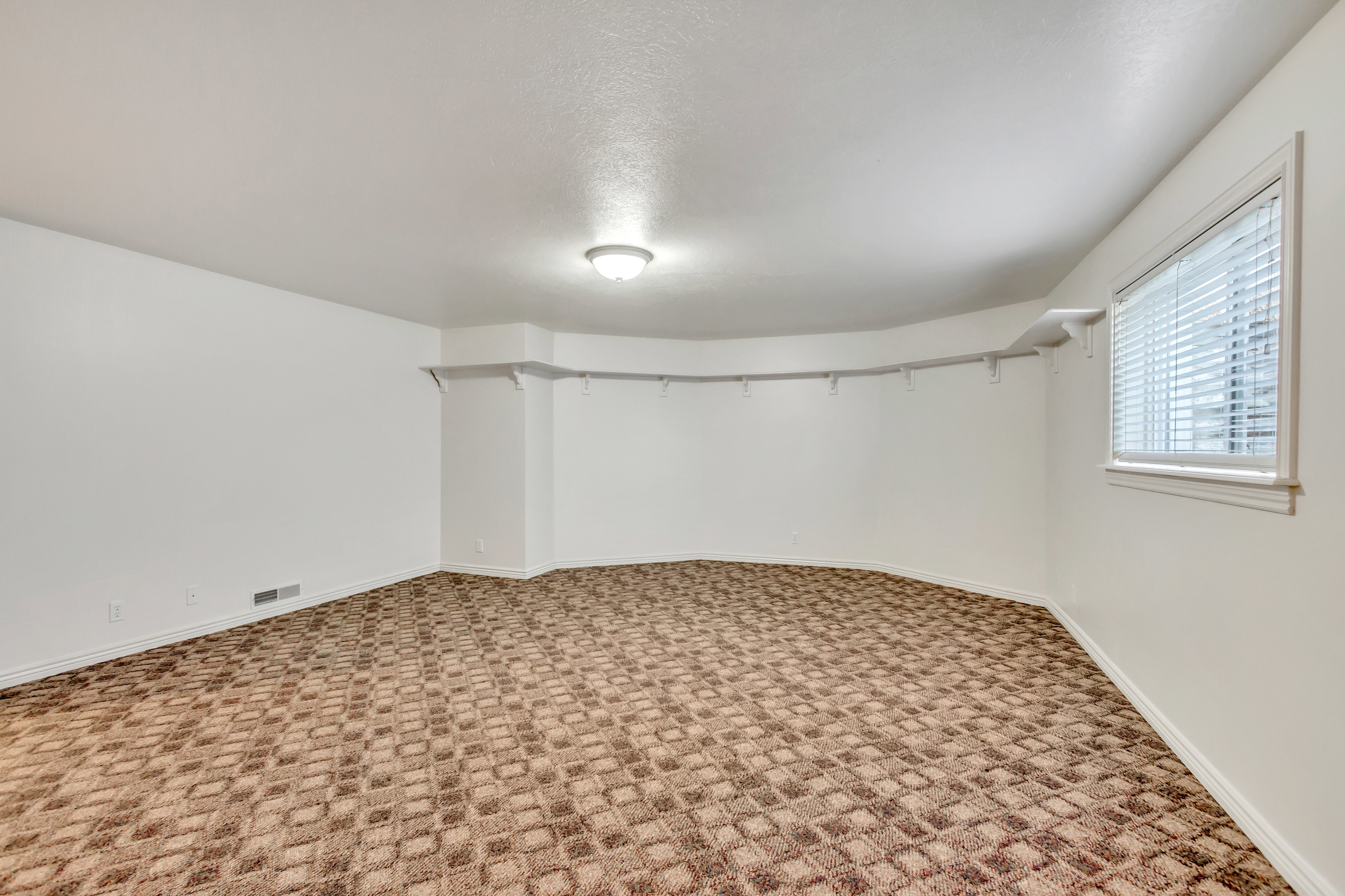 Spacious room featuring patterned carpeting, white painted walls, and a single window with blinds