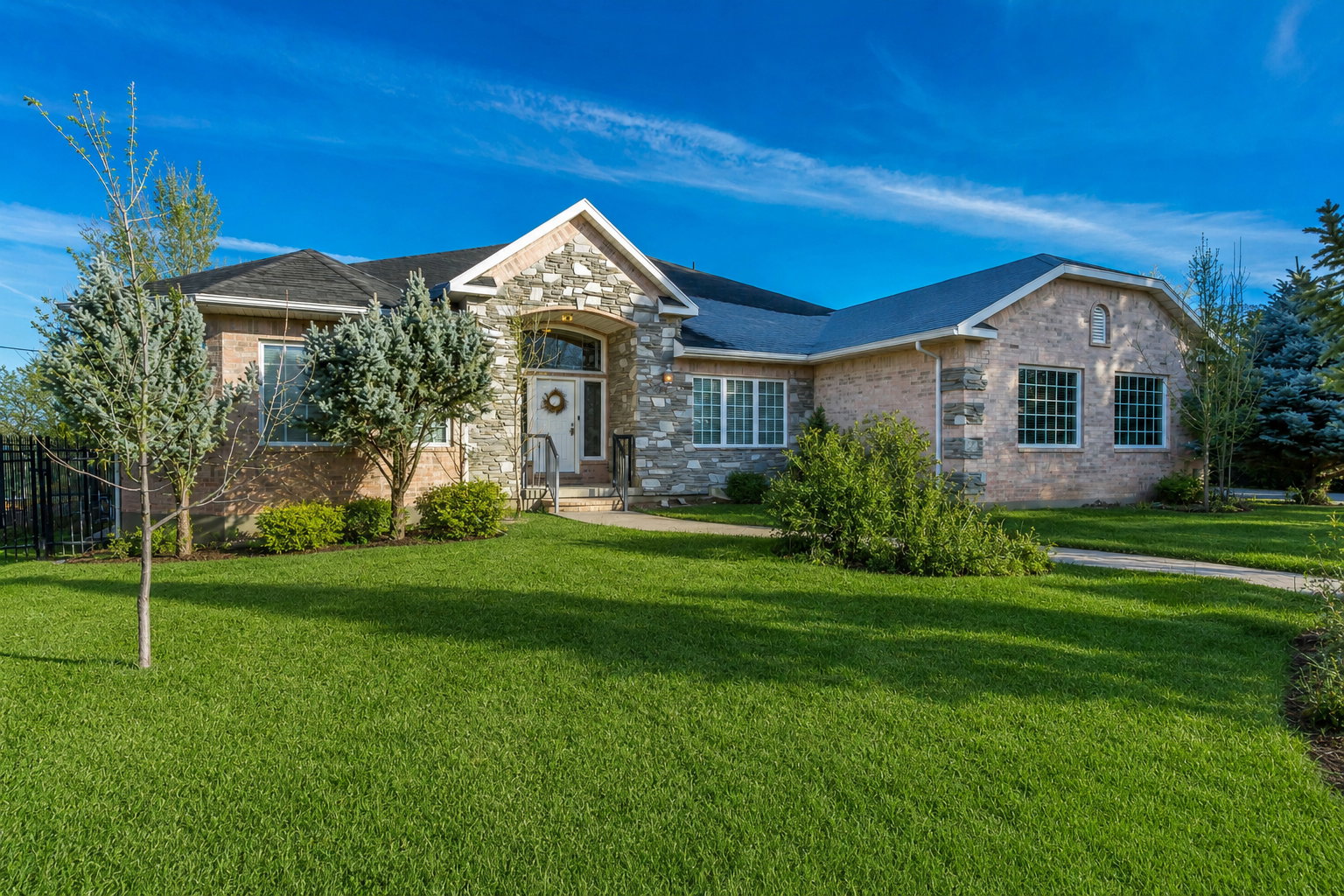 Spacious single-story residence featuring a stone and brick façade, a gabled entry with an arched portico, multiple window styles, a dark shingle roof, and a verdant front lawn
