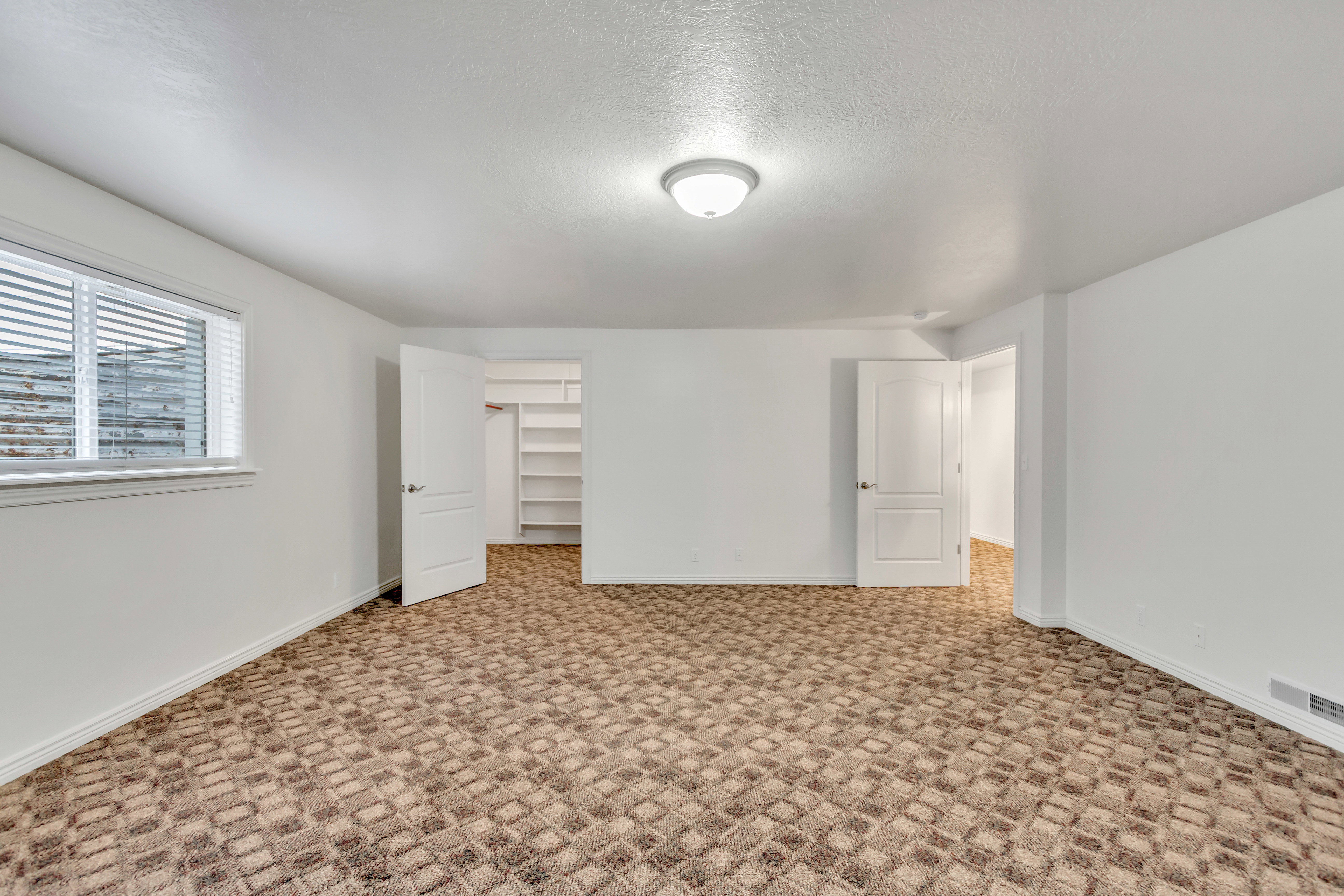 Spacious room featuring patterned carpet flooring, white walls, and a window with blinds