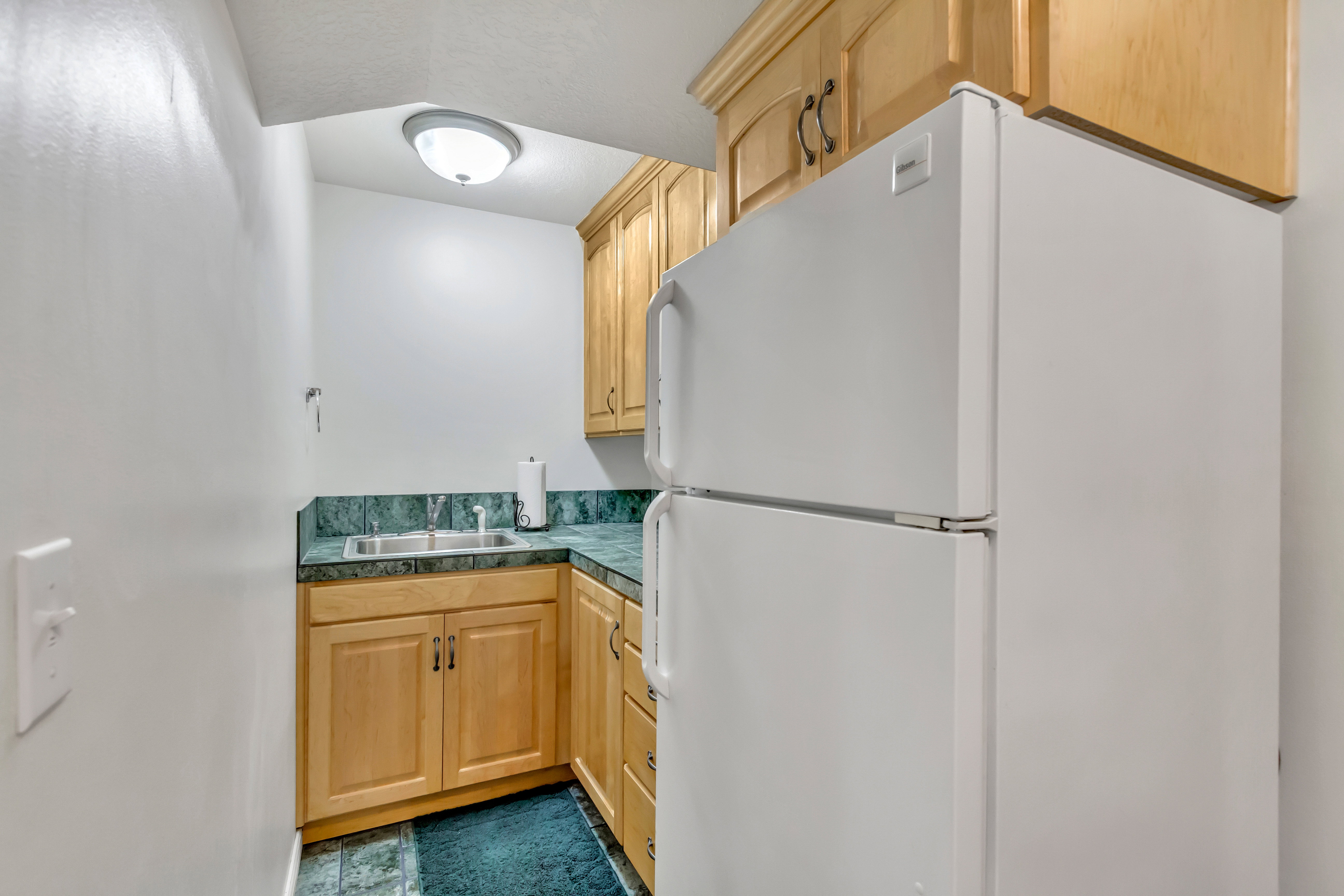 Compact kitchen area featuring a built-in stainless steel sink, wood-finish cabinetry, and green stone-look countertops