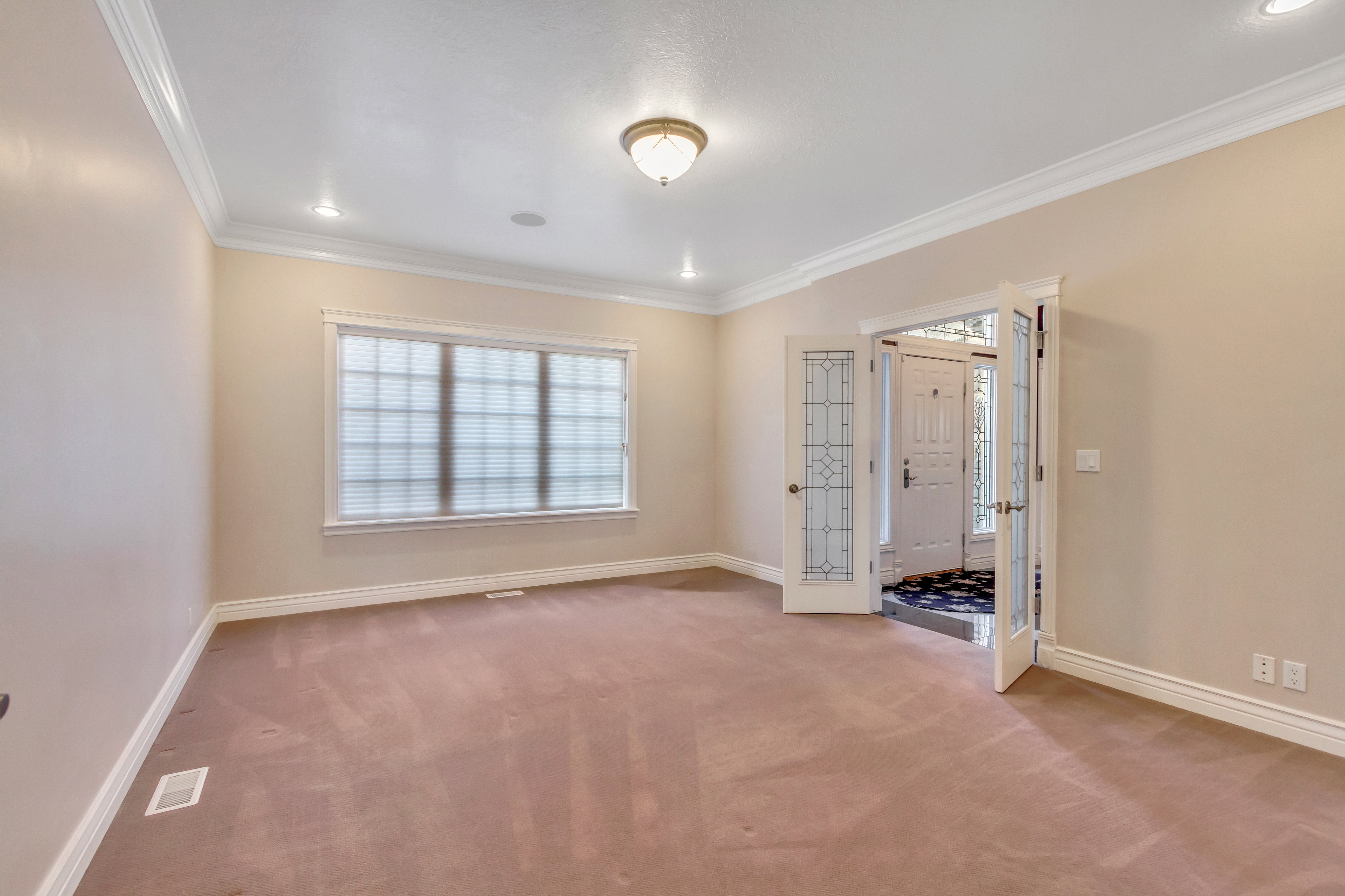 Spacious room featuring neutral wall paint, crown molding, recessed lighting, and a prominent window with blinds