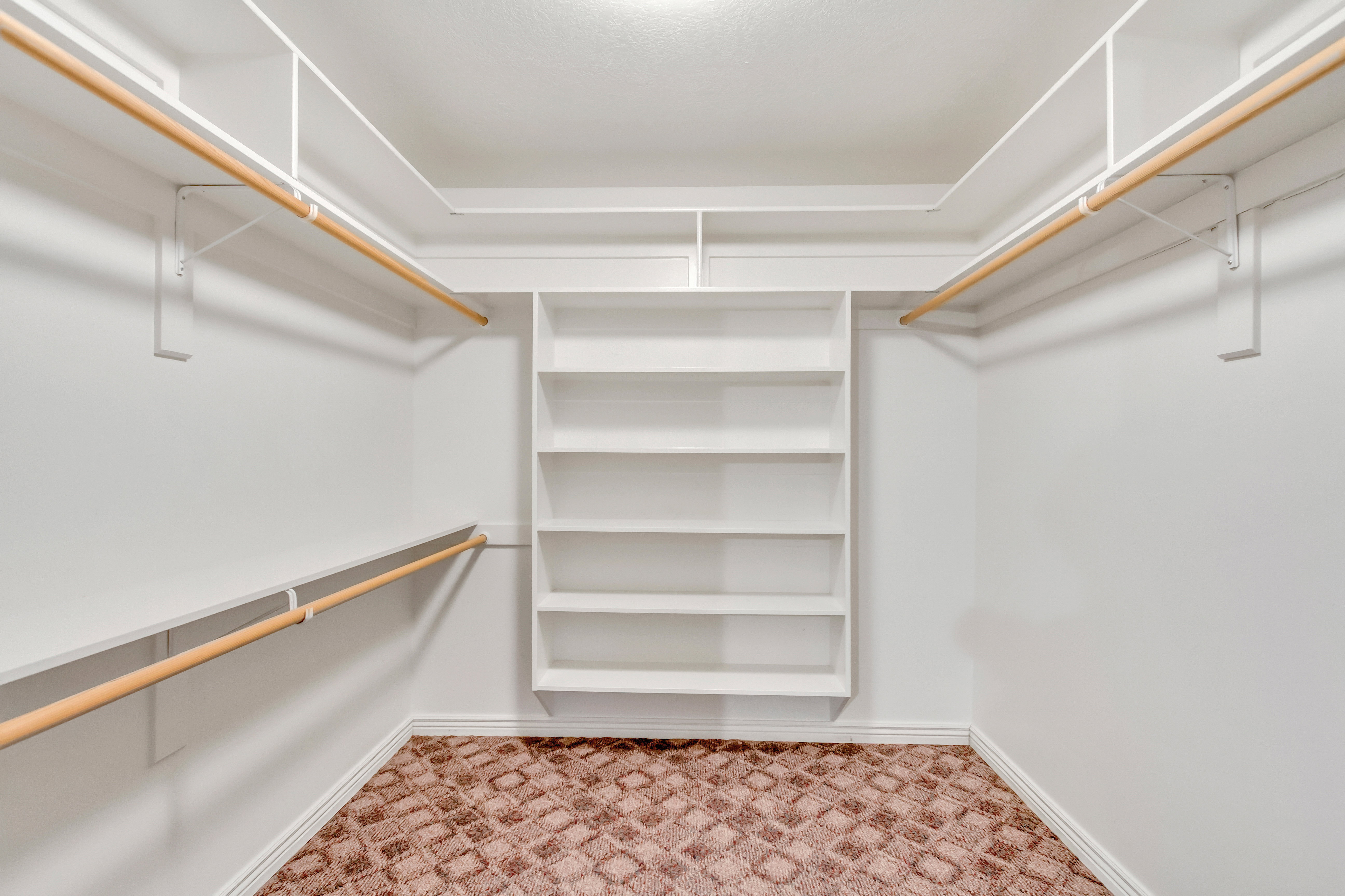 Walk-in closet featuring built-in shelving, multiple hanging rods, white walls, and patterned carpeting