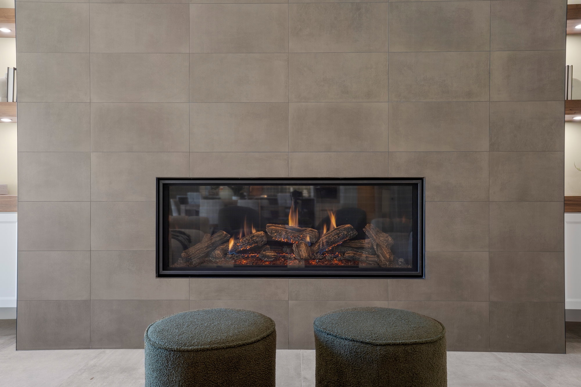 Modern fireplace featuring a wide glass-front insert with realistic log features, set within a large-format tile surround