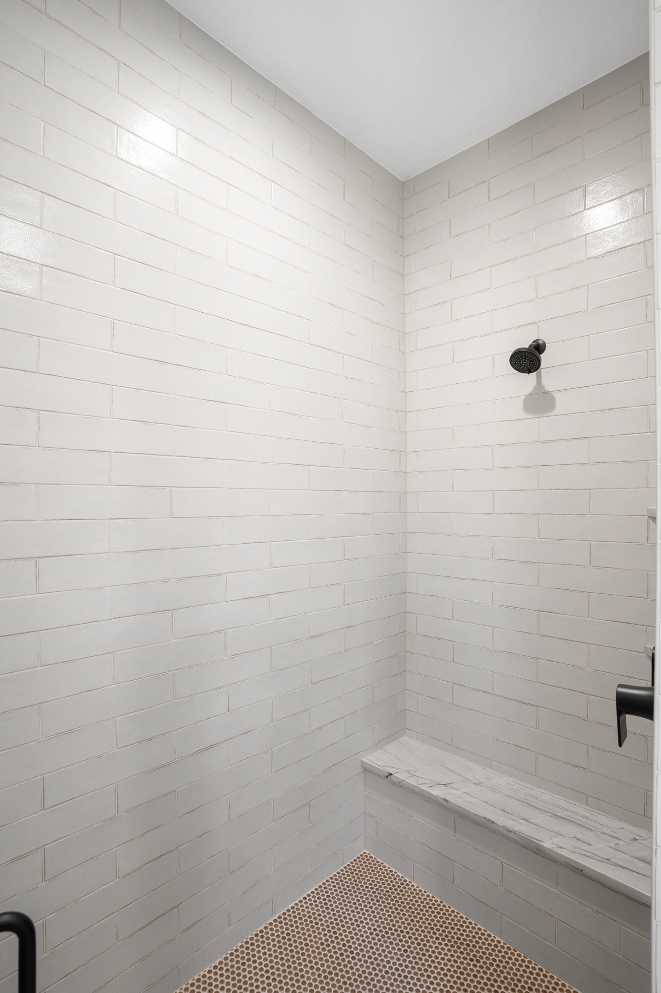 Shower stall featuring white subway tile, a built-in stone bench, a matte black shower head, and a coordinating matte black control handle