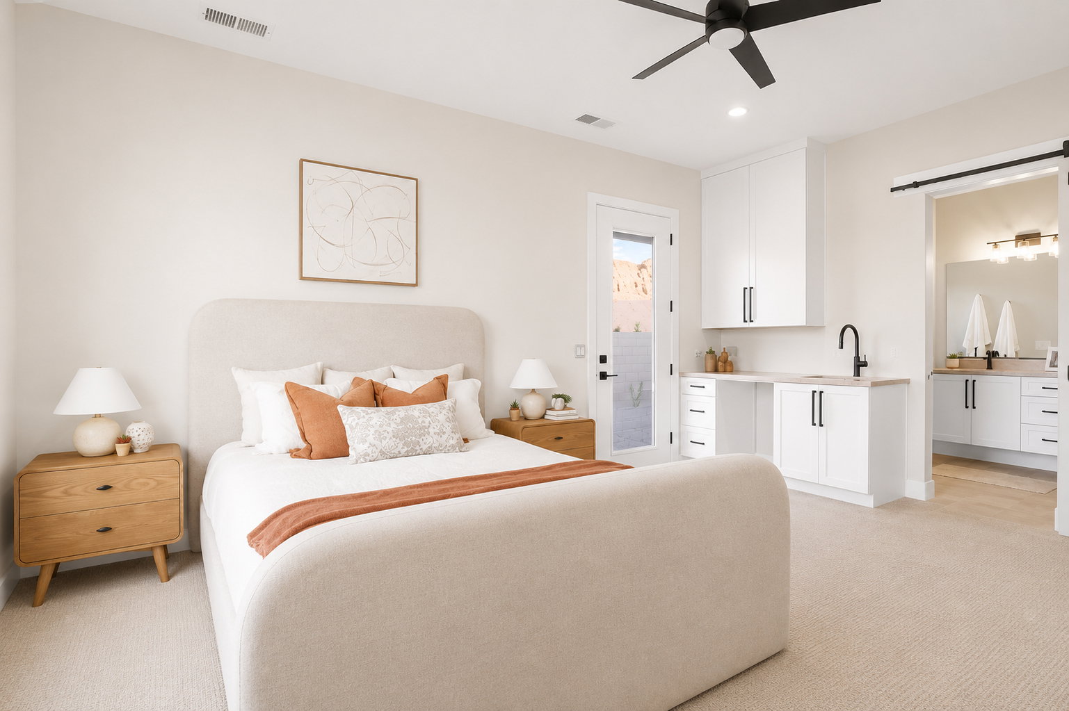 Spacious bedroom featuring light-toned carpeting, a ceiling fan, and a built-in wet bar with white cabinetry and a black faucet