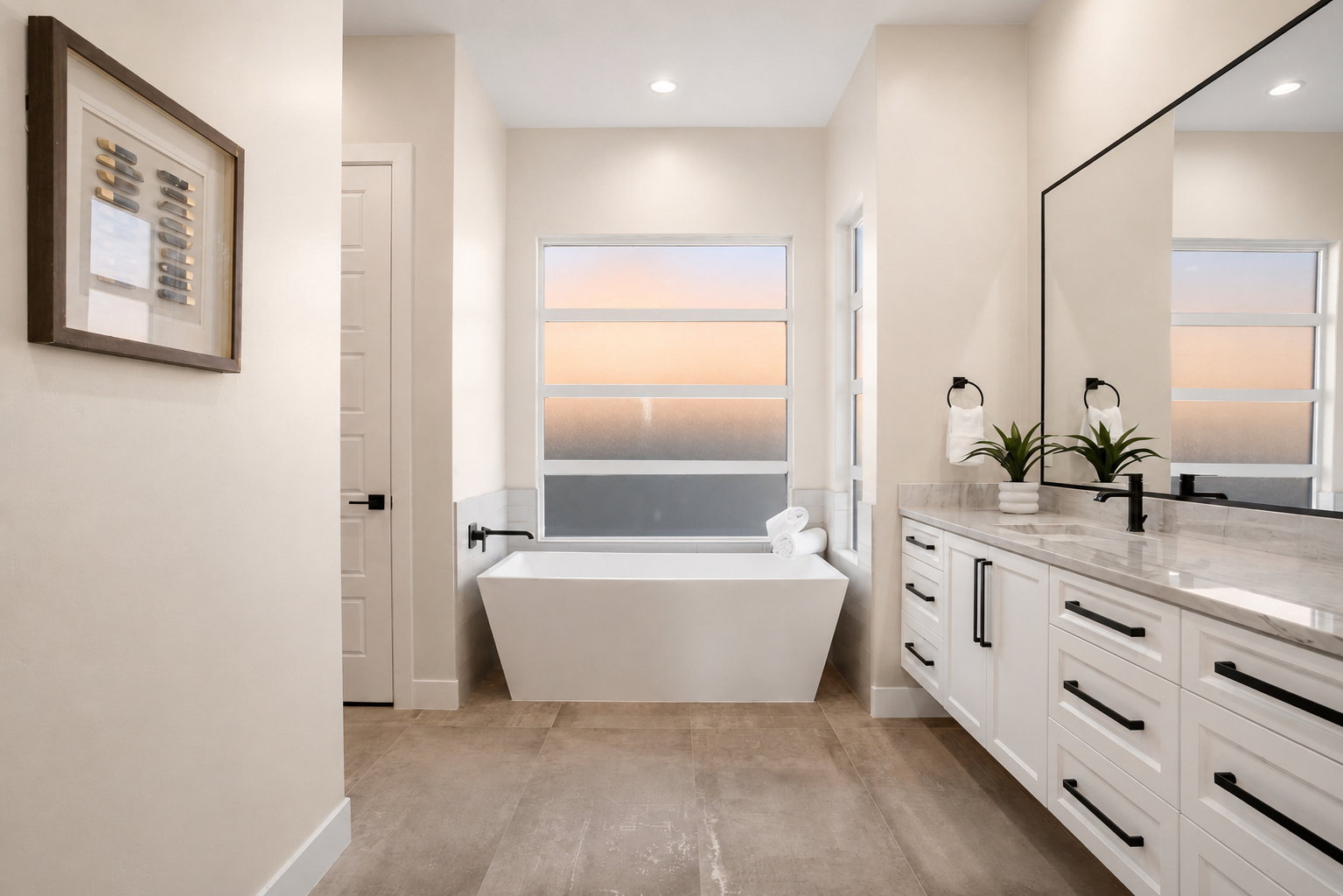 Bathroom featuring a freestanding soaking tub, dual-sink vanity with stone countertop, large rectangular mirror, and matte black fixtures