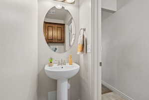 Pedestal sink with chrome faucet, an oval wall-mounted mirror, and overhead vanity lighting