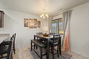 Spacious dining area featuring tile flooring, light neutral paint, chandelier, and large window overlooking covered back patio