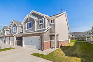 Contemporary townhome exterior featuring gray horizontal siding, red brick accents, an attached two-car garage, white trim, and a manicured lawn