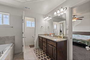 Primary bathroom featuring separate soaker tub and shower with tile surrounds, tile flooring, dual sink vanity with dark wood cabinetry and granite countertops
