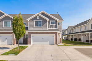 Modern townhome exterior featuring gray siding, brick accents, white trim, and a two-car garage