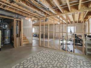 Unfinished basement featuring exposed wood framing, concrete flooring, and visible utility infrastructure, including a water heater