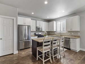Modern kitchen featuring white shaker cabinetry, stainless steel appliances, a center island with seating, granite countertops, and wood-finish flooring