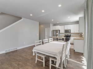Open-concept living space featuring wood-finish flooring, recessed lighting, and a white kitchen with stainless steel appliances