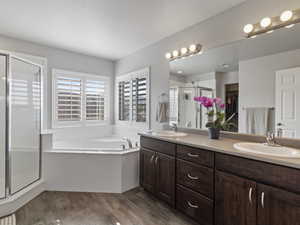 Luxurious bathroom featuring a corner soaking tub, separate glass-enclosed shower, dual vanities with wood-finish cabinetry, and wood-finish flooring