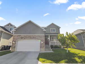 Contemporary exterior with stone veneer and stucco finishes, featuring an attached two-car garage, a covered front porch with white railings, and a well-maintained front lawn