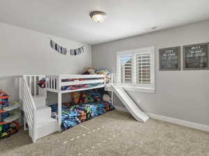 Carpeted room with a ceiling-mounted light fixture and a window featuring white plantation shutters