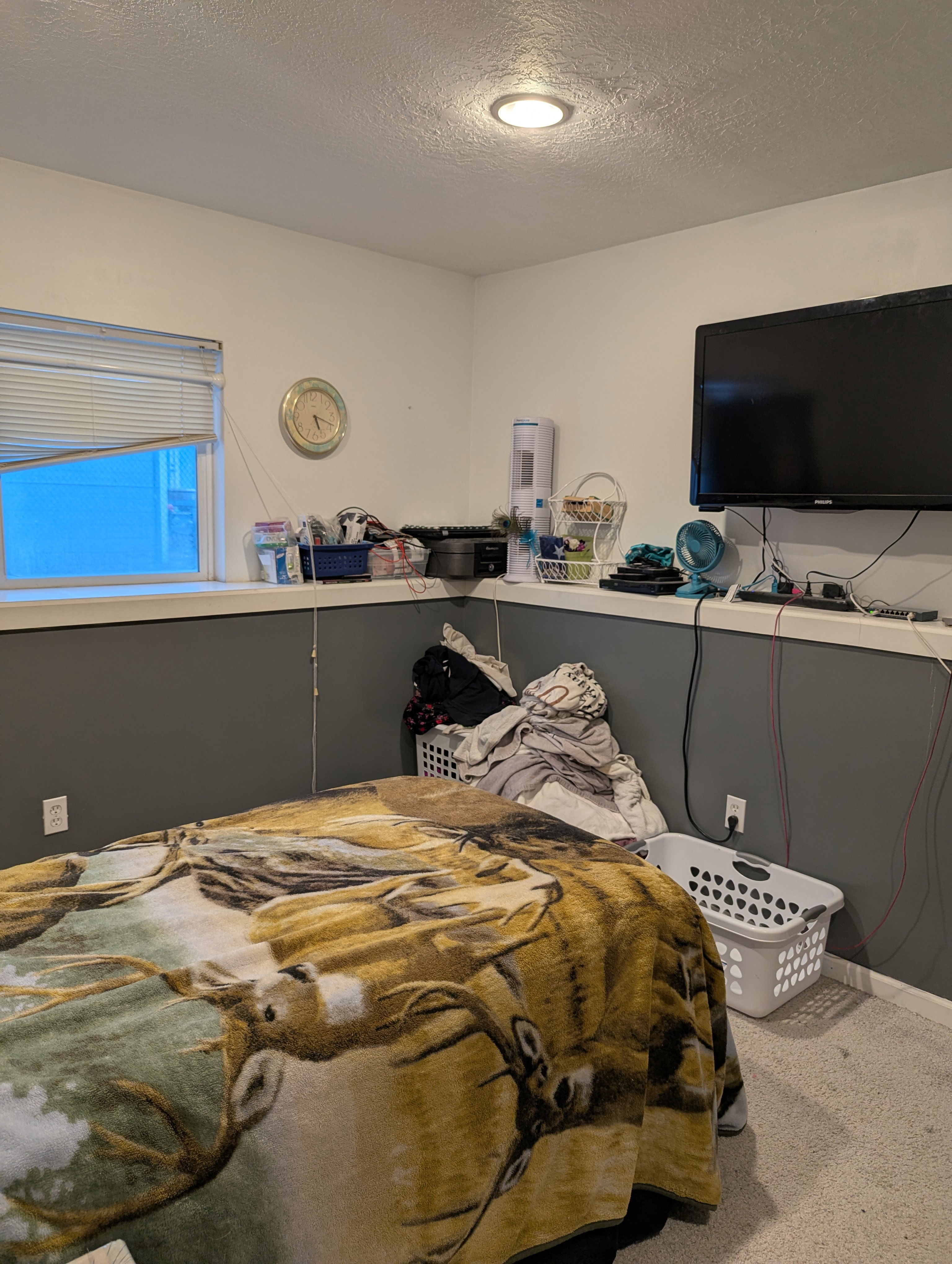 Recessed ceiling lighting illuminates a room featuring a window with horizontal blinds, a mounted television, and a carpeted floor