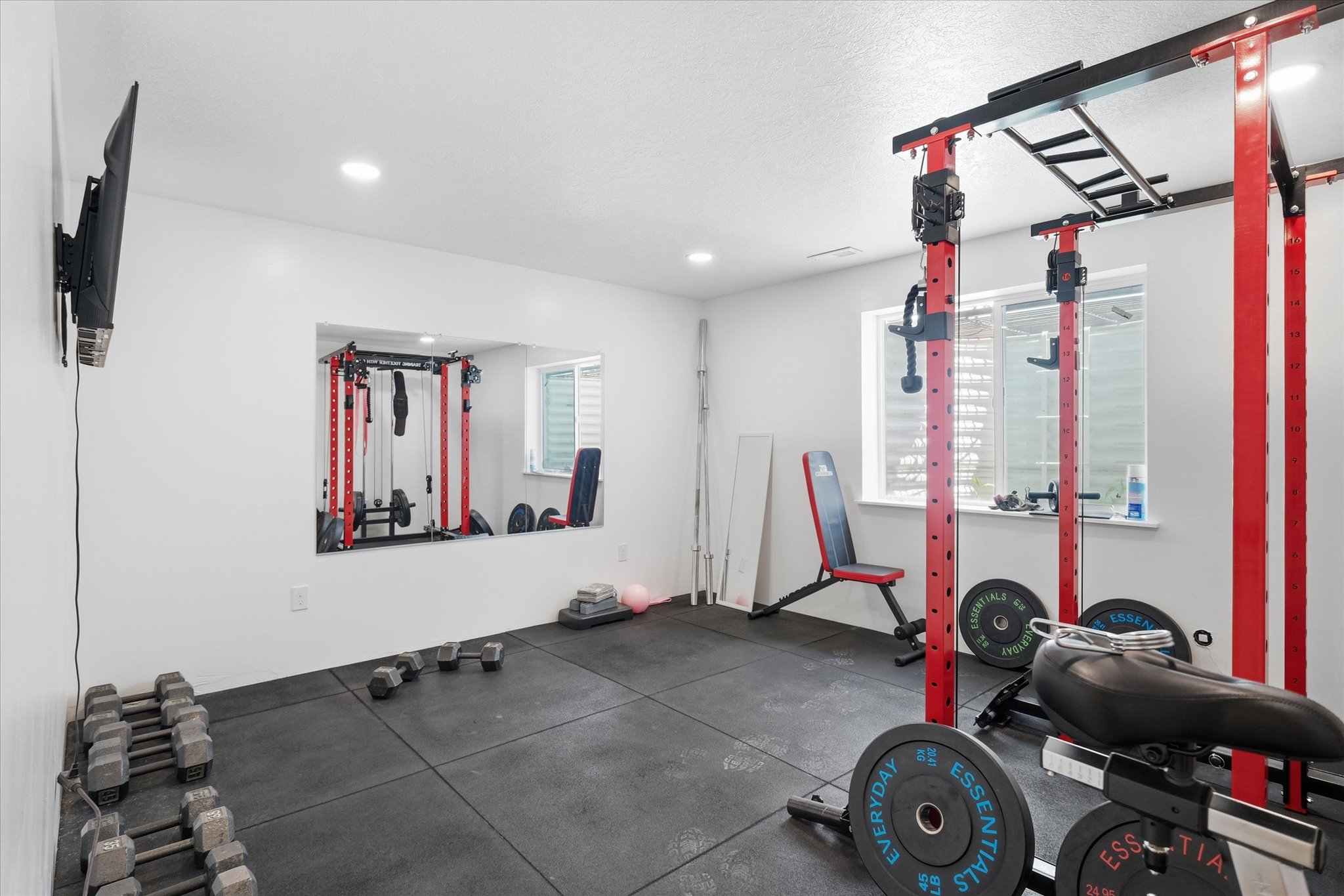 Dedicated fitness space featuring rubberized flooring, recessed lighting, a built-in wall mirror, and a window with horizontal blinds